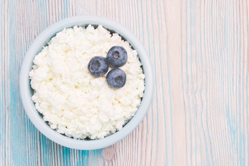 An overhead photo of fresh natural cottage cheese with blueberries in a ceramic bowl on the wooden table. Organic eco healthy meal, dairy product. Top view. Place for text, copyspace.