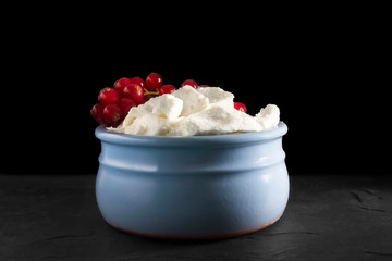 Photo of fresh natural cottage cheese with red currant in a blue ceramic bowl on the black stone plate. Organic eco healthy meal, dairy product. Place for text, copyspace.