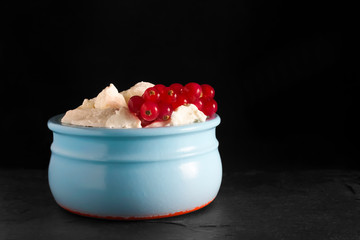 Photo of fresh natural cottage cheese with red currant in a blue ceramic bowl on the black stone plate. Organic eco healthy meal, dairy product. Place for text, copyspace.