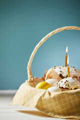 Fototapeta na wymiar easter cakes with chicken eggs and napkin in wicker basket on turquoise with copy space