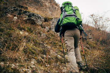 Naklejka premium Horizontal image of traveler bearded man trekking and mountaineering during his journey. Rear view of young male hiking in mountains. Travel, people, sport and healthy lifestyle concept