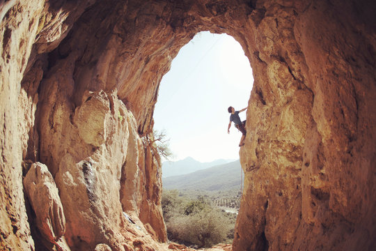 Male rock climber hanging with one hand on challenging route on cliff and putting chalk on another