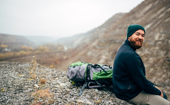 Rear view image of happy hiker young man in green hat, feel good after hiking in mountains. Traveler bearded male smiling and feel happy during trekking in his journey. Travel, lifestyle