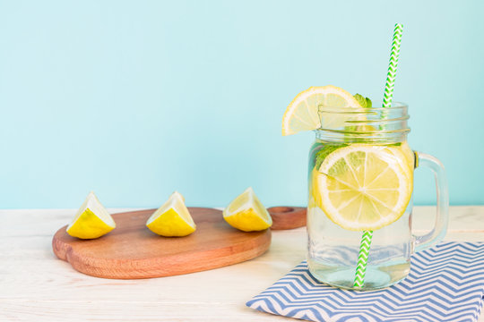 Citrus lemonade water with sliced lemon and mint, healthy and detox water drink in summer on wooden table with blue lighten background