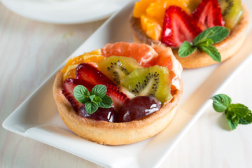 Fresh fruit and berry tart dessert with toss sugar on wooden background. Delicious sweet cake with raspberries, grapes, strawberries, cherry, kiwi, grapefruit and cream.