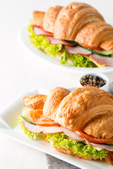 Fresh croissant or sandwich with salad, ham, jamon, prosciutto, salami, cheese, chicken, tomatoes on wooden background. Morning breakfast concept. Healthy and fast food.