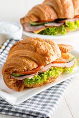 Fresh croissant or sandwich with salad, ham, jamon, prosciutto, salami, cheese, chicken, tomatoes on wooden background. Morning breakfast concept. Healthy and fast food.