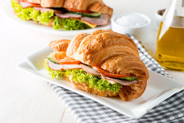 Fresh croissant or sandwich with salad, ham, jamon, prosciutto, salami, cheese, chicken, tomatoes on wooden background. Morning breakfast concept. Healthy and fast food.