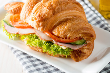 Fresh croissant or sandwich with salad, ham, jamon, prosciutto, salami, cheese, chicken, tomatoes on wooden background. Morning breakfast concept. Healthy and fast food.