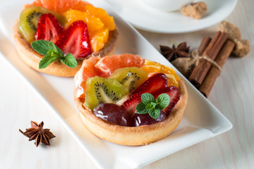 Fresh fruit and berry tart dessert with toss sugar on wooden background. Delicious sweet cake with raspberries, grapes, strawberries, cherry, kiwi, grapefruit and cream.