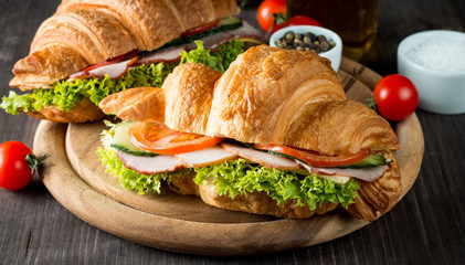 Fresh croissant or sandwich with salad, ham, jamon, prosciutto, salami, cheese, chicken, tomatoes on wooden background. Morning breakfast concept. Healthy and fast food.