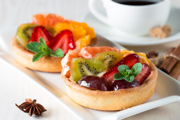 Fresh fruit and berry tart dessert with toss sugar on wooden background. Delicious sweet cake with raspberries, grapes, strawberries, cherry, kiwi, grapefruit and cream.