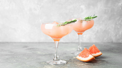 Drink grapefruit rosemary and ice two elegant glass goblets on gray concrete background. A refreshing summer cocktail.