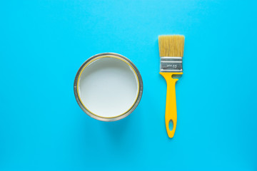 Jar with white paint and yellow brush on blue background. Top view.  Renovation concept. 