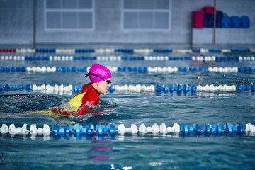 Female athlete in a red-yellow swimsuit is swimming in the style of breaststroke. Splashes of water...