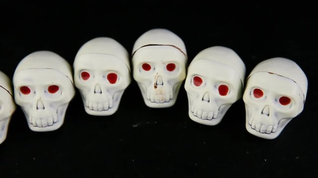 panorama view row of white chocolate candies in skeleton skull shape with red eyes served on black background