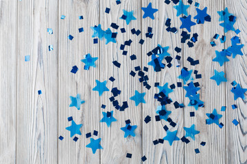 blue shiny stars on a wooden background abstraction. Abstract colorful background with blue elements on a light background. Top view of a train of confetti blue stars on a wooden  background