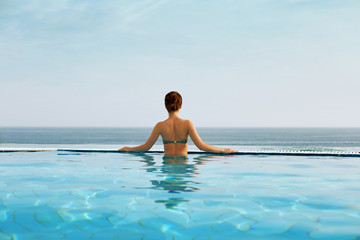 Luxury vacation travel woman relaxing in infinity swimming pool on summer beach resort.  Spa relaxation watching  in nature landscape background.