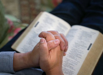 Praying : male hands clasped together on an open bible