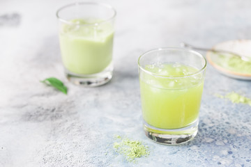 Iced Matcha green latte in glasses with matcha powder on light background.