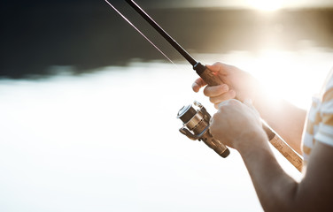 Midsection of a man fishing by a lake, holding a rod. A close-up.