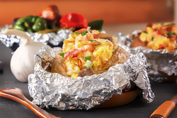 Baked potato in foil with bacon, onions and mushrooms on a gray wooden table. Close-up
