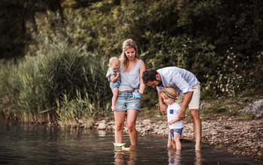 Young family with two toddler children outdoors by the river in summer, playing.
