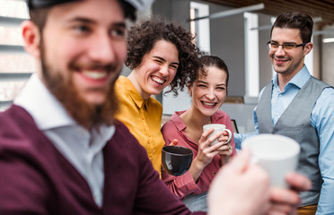 A group of young businesspeople with cup of coffee standing in office.