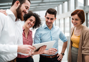 Group of young busiensspeople with tablet standing in office, talking.