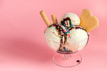 scoops of vanilla flavor ice cream in glass bowl with chocolate sauce, strewed sprinkles and waffle...