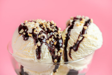 close up of scoops vanilla ice cream decorated chocolate topping and nuts on pink background