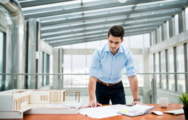 Young businessman or architect with model of a house standing in office, working.