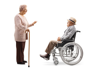 Elderly man sitting in a wheelchair and listening to a senior woman talking and standing with a cane