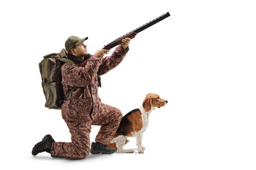Hunter kneeling with a shotgun, aiming upwards and a beagle dog next to him