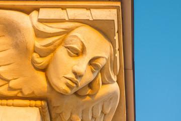 Stucco Sculpture of a Female Mask with Wings as a Decorative Element of the Building Against Blue Sky at Sunset