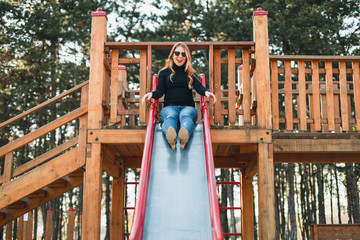 Young happy woman enjoying on the slide in the public playground