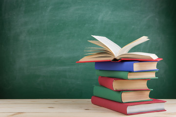 Education and reading concept - group of colorful books on the wooden table in the classroom, blackboard background