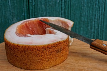 one long piece of fresh pork lard and a knife lay on a brown wooden plank against a green wall