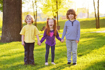 Fototapeta premium a group of small children smiling holding hands on a background of grass, a tree and a park. Children's Day, June 1, friendship, childhood.