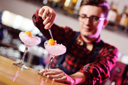 a young bartender prepares a cocktail on the background of the bar. Bartender show