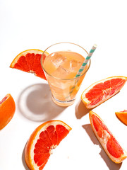 Slices of juicy grapefruit and a glass of fresh lemonade with ice on a white background.