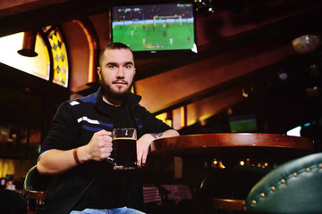 young attractive bearded man drinking beer in pub and watching football