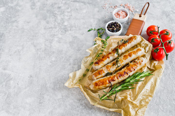 Fried sausages on a wooden chopping Board, rosemary, thyme, cherry tomatoes. Gray background, top view