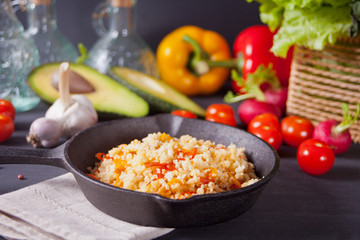 Delicious homemade vegetarian couscous with tomatoes, carrots, pepper and fresh basil on a dark kitchen table with vegetables on the background