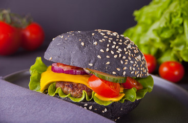 Homemade black burger with cutlet and vegetables on the napkin