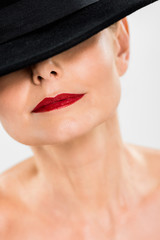 selective focus of middle aged elegant and fashionable woman with red lips in black hat isolated on grey