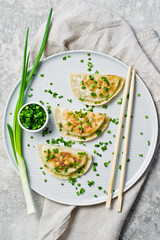 Homemade Korean dumplings, chopsticks, fresh green onions. Gray background, top view