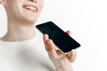 Indoor portrait of attractive young man isolated on gray background, holding smartphone, using voice control, feeling happy and surprised. Human emotions, facial expression concept.