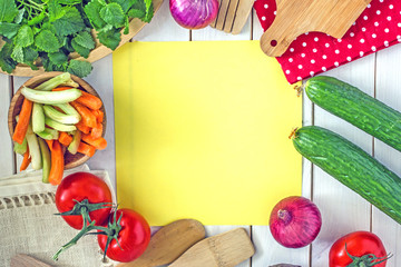 Culinary background. The light wooden surface on it is a yellow lettering sheet, around fresh vegetables, greens, items for cooking. copy space top view