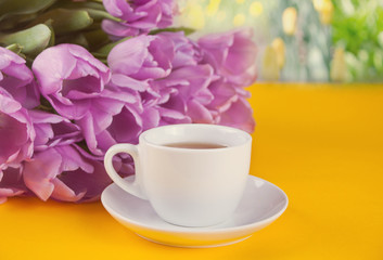 Obraz na płótnie Canvas A cup of tea and violet tulips on the table